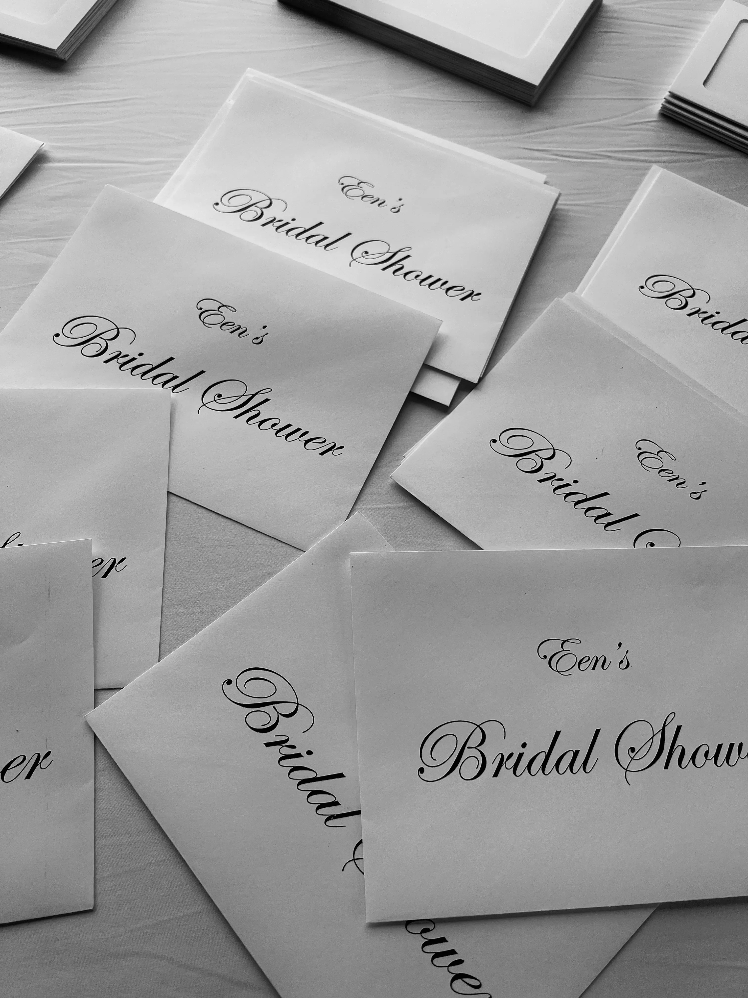 Black-and-white flat lay of bridal shower invitation envelopes fanned across a table.