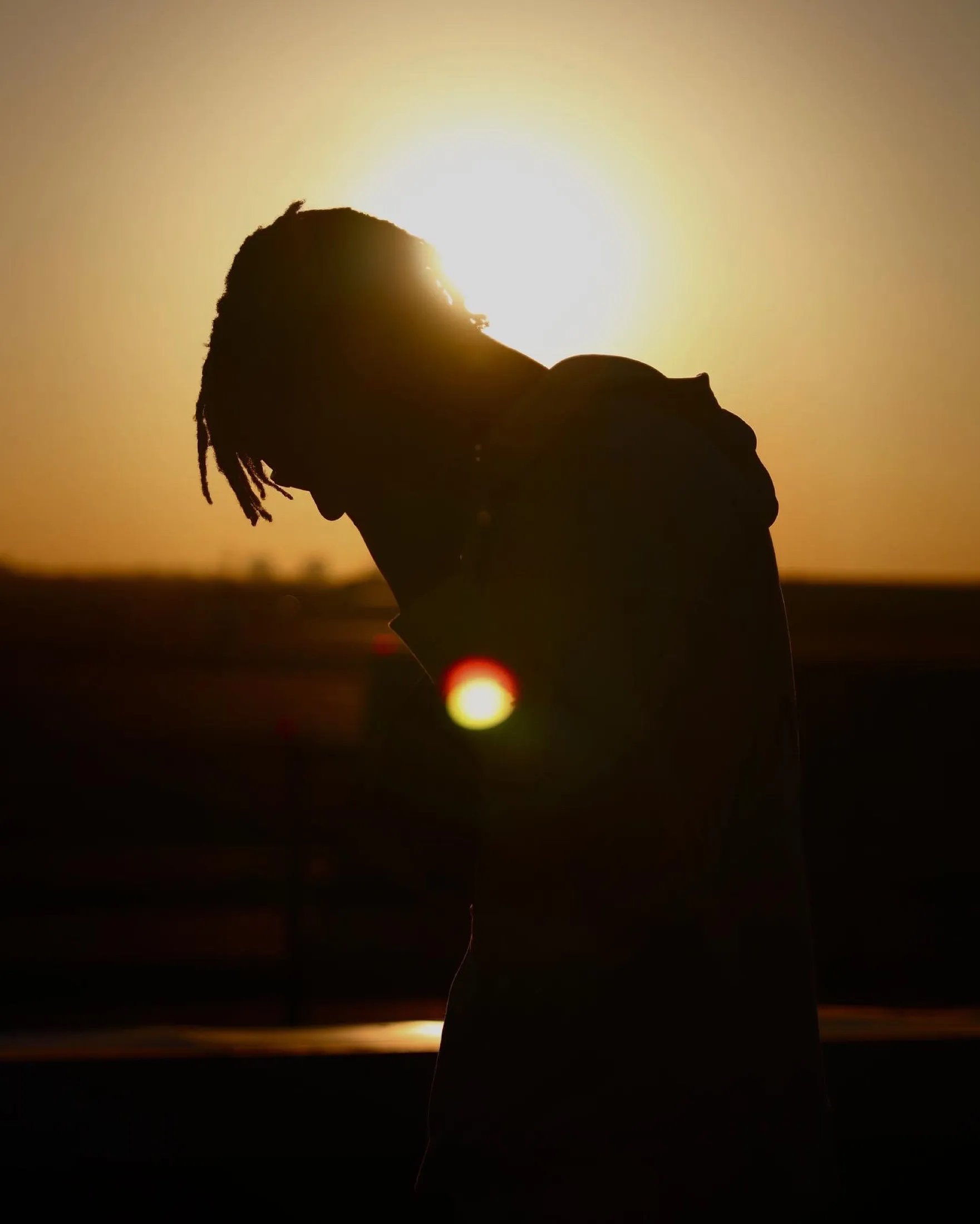 Silhouetted figure at sunset with strong lens flare.