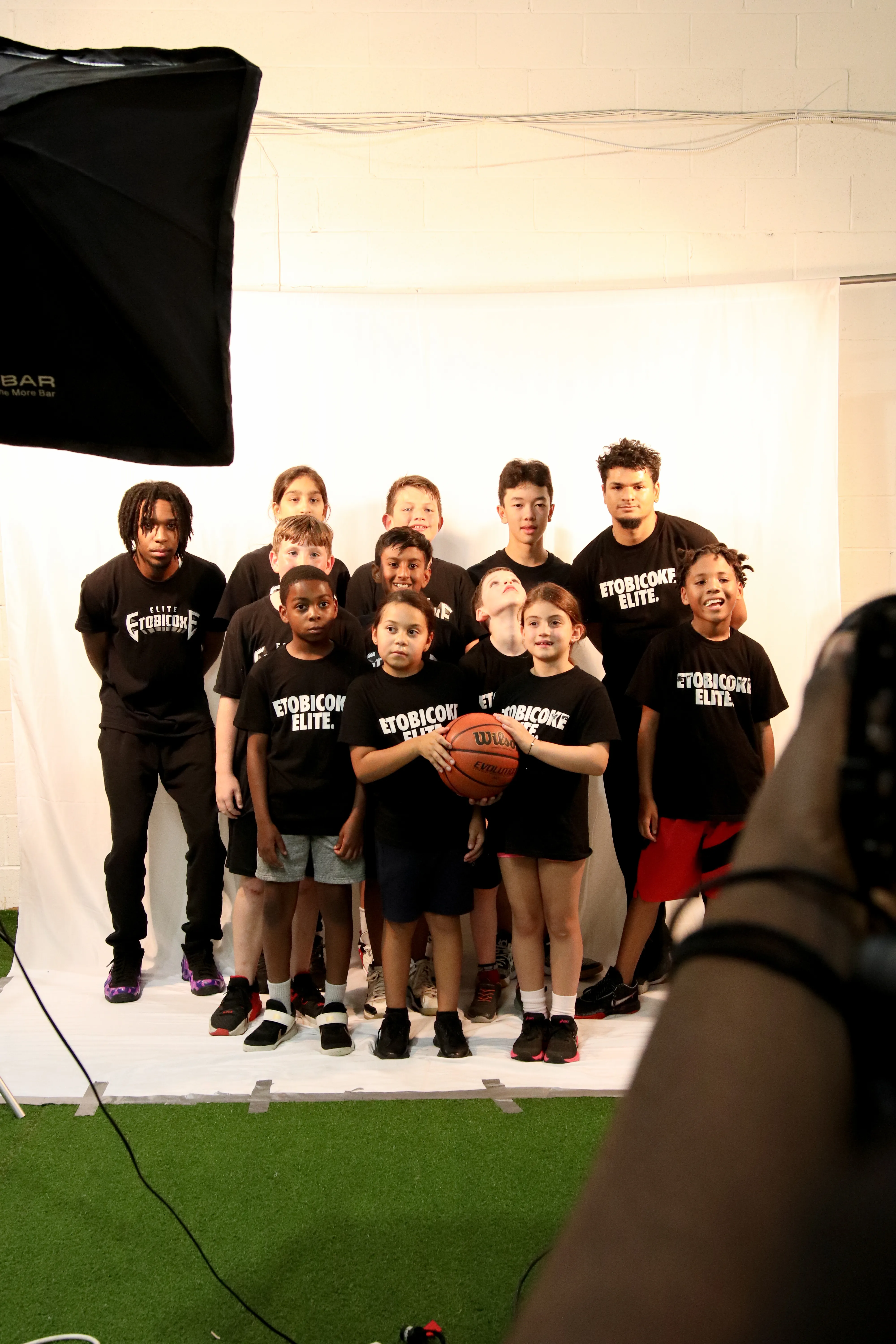 Youth basketball team and coach posing in matching branded T-shirts for a studio group photo.