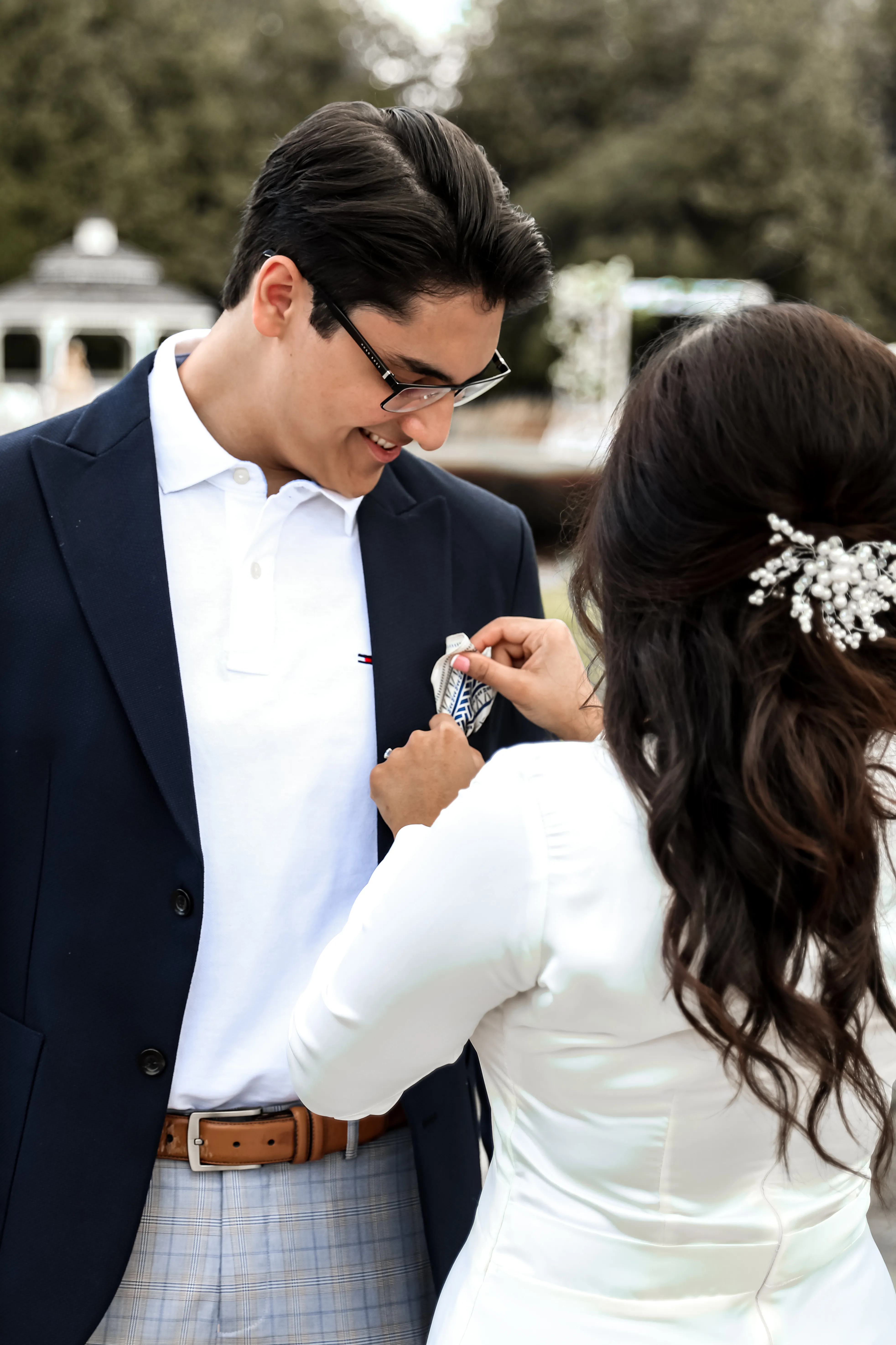 Bride pinning a boutonniere on the groom’s lapel outdoors.